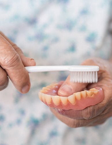 Patient using toothbrush to clean dentures