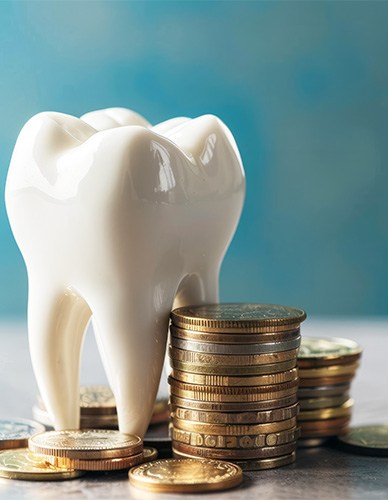 A large fake tooth next to a pile of coins on a gray surface with blue background