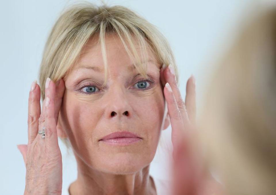 Woman looking in mirror, concerned about signs of aging