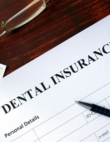 Corner of dental insurance form with pen and gold framed glasses