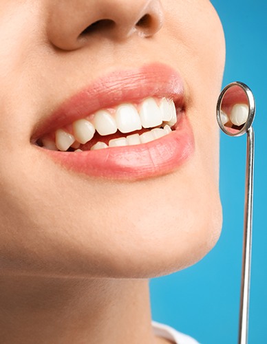 Nose-to-chin view of a woman smiling holding dental  mirror to teeth with blue background