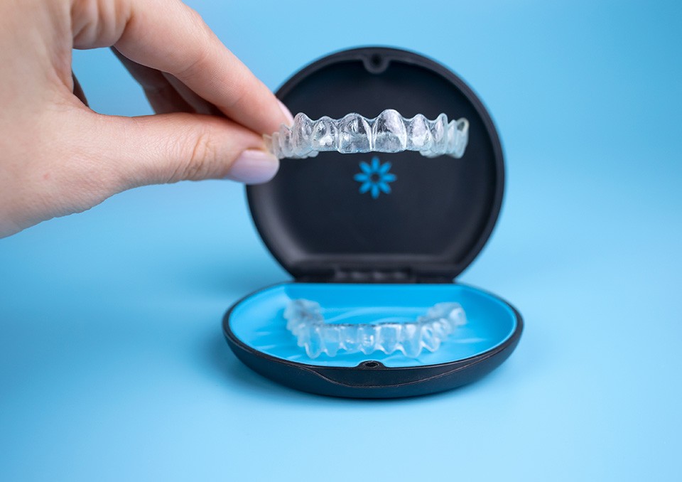 Someone lifting Invisalign tray from its case with light blue background