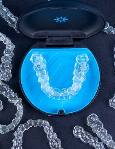 Several Invisalign trays surrounding one in the case with a black background