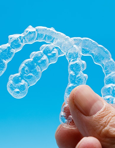 Someone holding two clear aligners up to a sky blue background