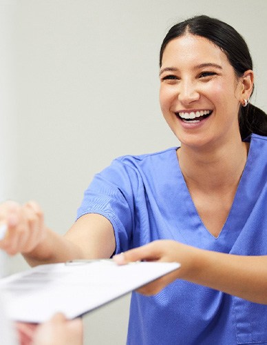 Dentist in blue scrubs handing paperwork on clipboard to patient