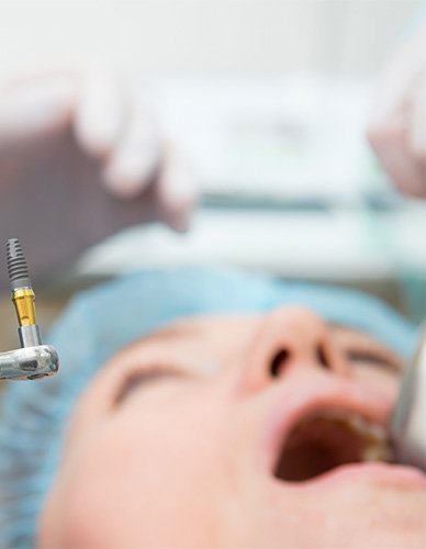 Dentist holding up a metal implant rod with patient blurry in background