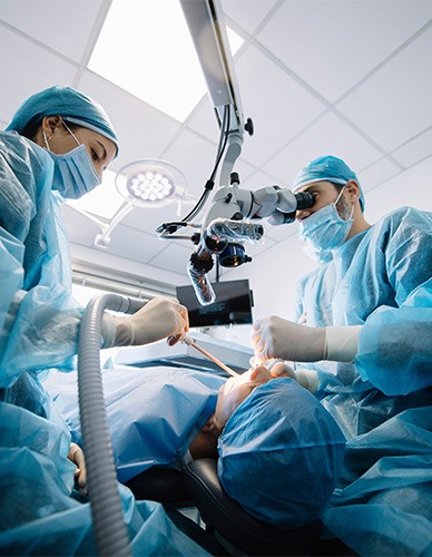 Two dentists in blue scrubs performing surgery on patient